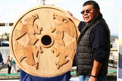 Coast Salish artist Butch Dick standing next to a Signs of Lekwungen cedar carving