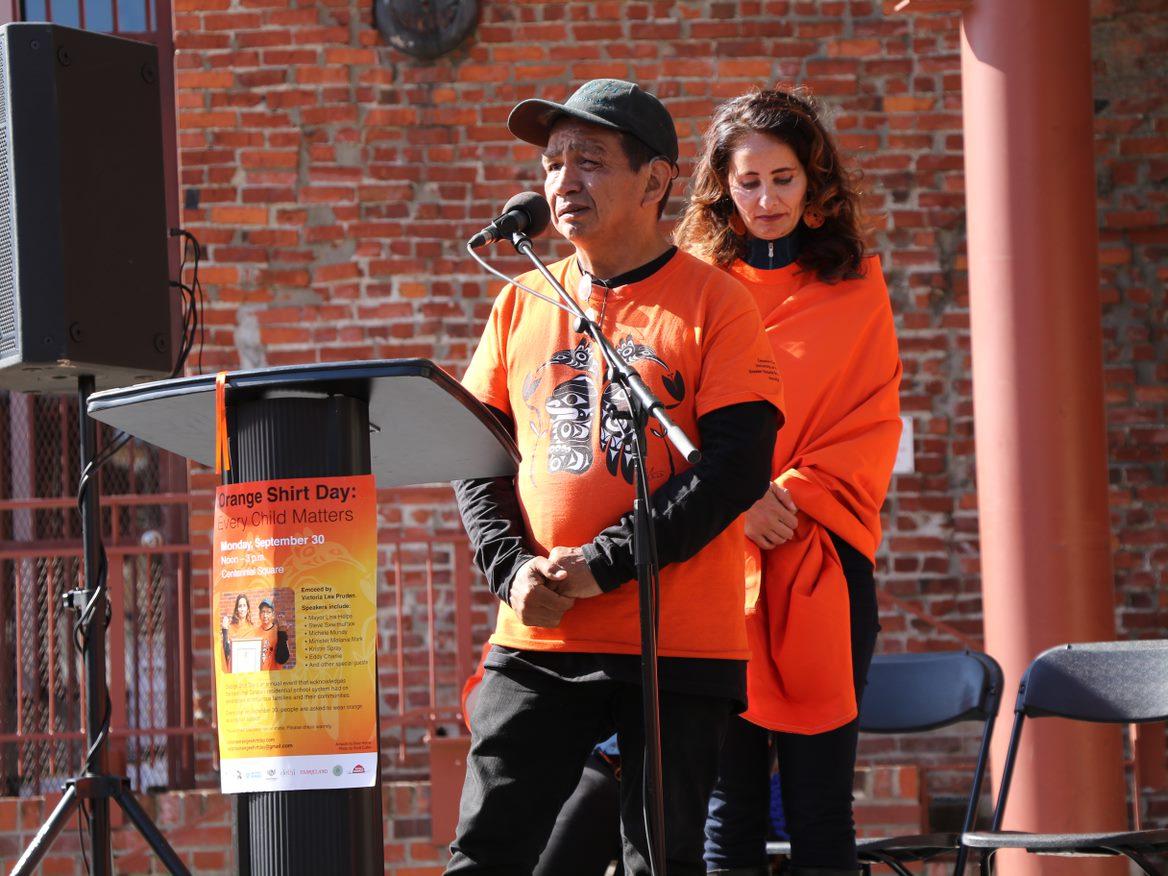 Eddy Charlie speaking at the Victoria Orange Shirt Day Ceremony in Centennial Square. Friend Kristin Spray is standing behind Eddy.